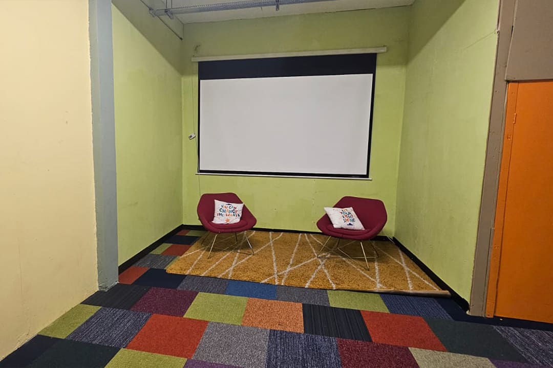 The Creative Breakout Space with a colourful patterned carpet, red armchairs and a projector screen.